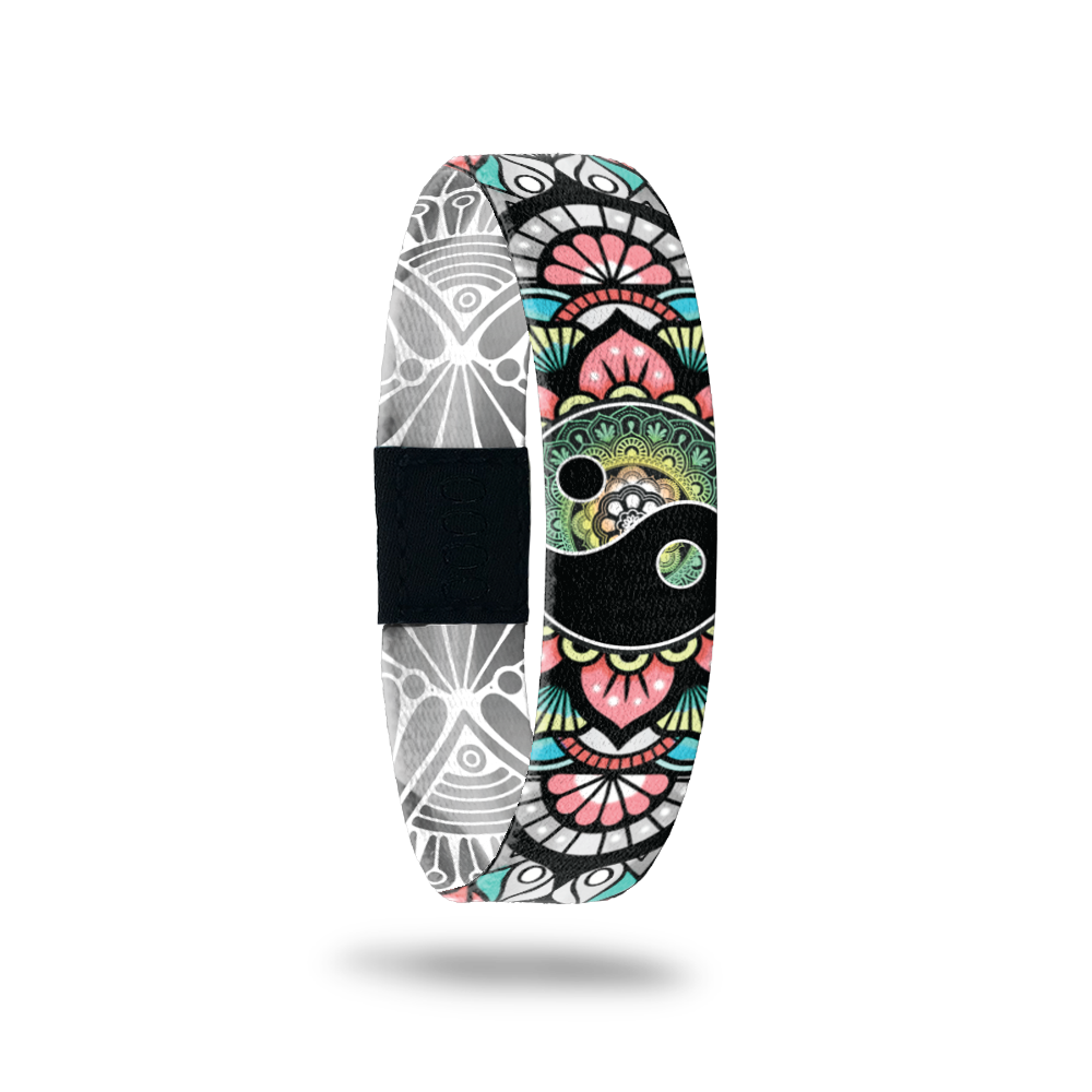 This is a reversible wristband. The outside is muted multicolors of a paisly deign with green, pink, teal and grey. It has a ying-yang in the center of the design. The inside is all grey and white paisley design and says Balance. It can be worn with the design or the words on the outside. 