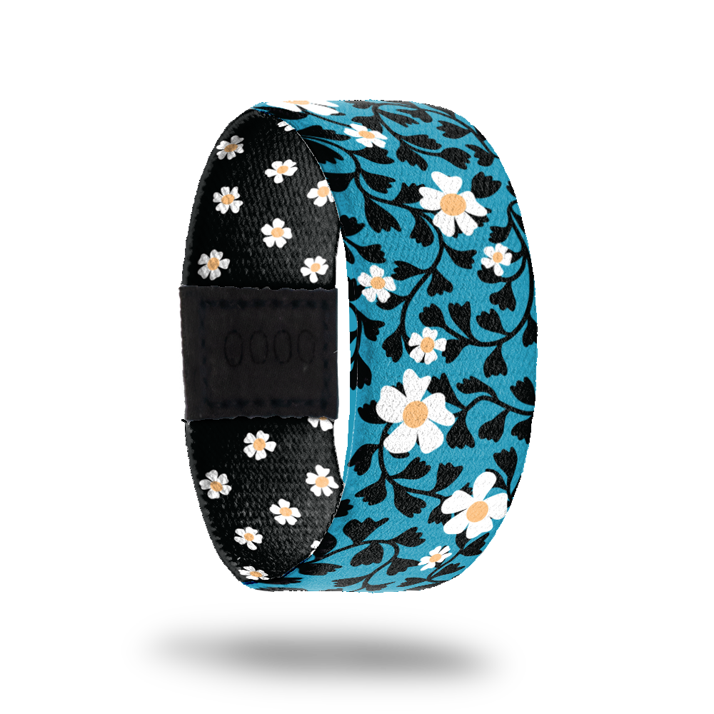 Wristband single that is bright blue with white daisies and black leaves all over. The inside is all black with white daises and reads Open Your Heart. 
