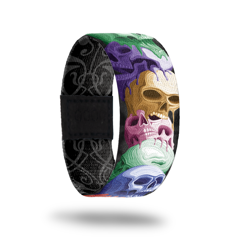 product image of front of wristband named Reflect. The design is a stack of hand drawn skulls in different colors such as purple, gold, pink, blue, and green