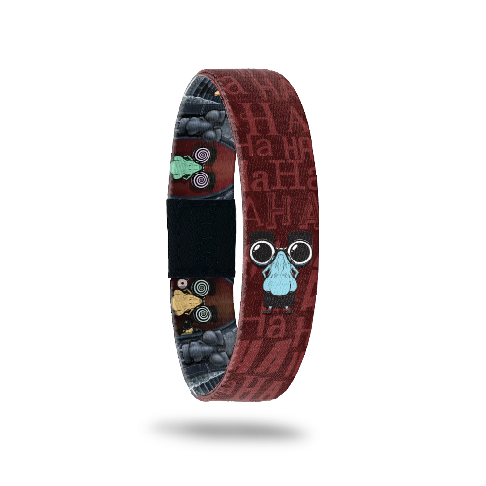 Brown and dark reddish bracelet with "HA HA" all around the design. Comes with a pin of a goofy big nose with mustache and glasses. Inside is the same goofy monster with glasses adn swirly eyes. 