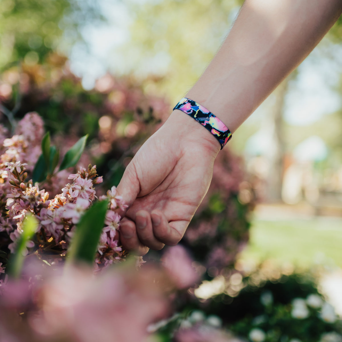 Lifestyle photo of hand holding flowers showing wrist with outside design of find bigger problems with neon geometric design overlaying a black background