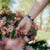 Lifestyle photo of hand holding flowers showing wrist with outside design of find bigger problems with neon geometric design overlaying a black background