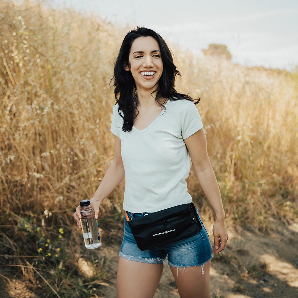 life style photo of a woman on a hike with the fanny pack around her waist with a water bottle in her hands