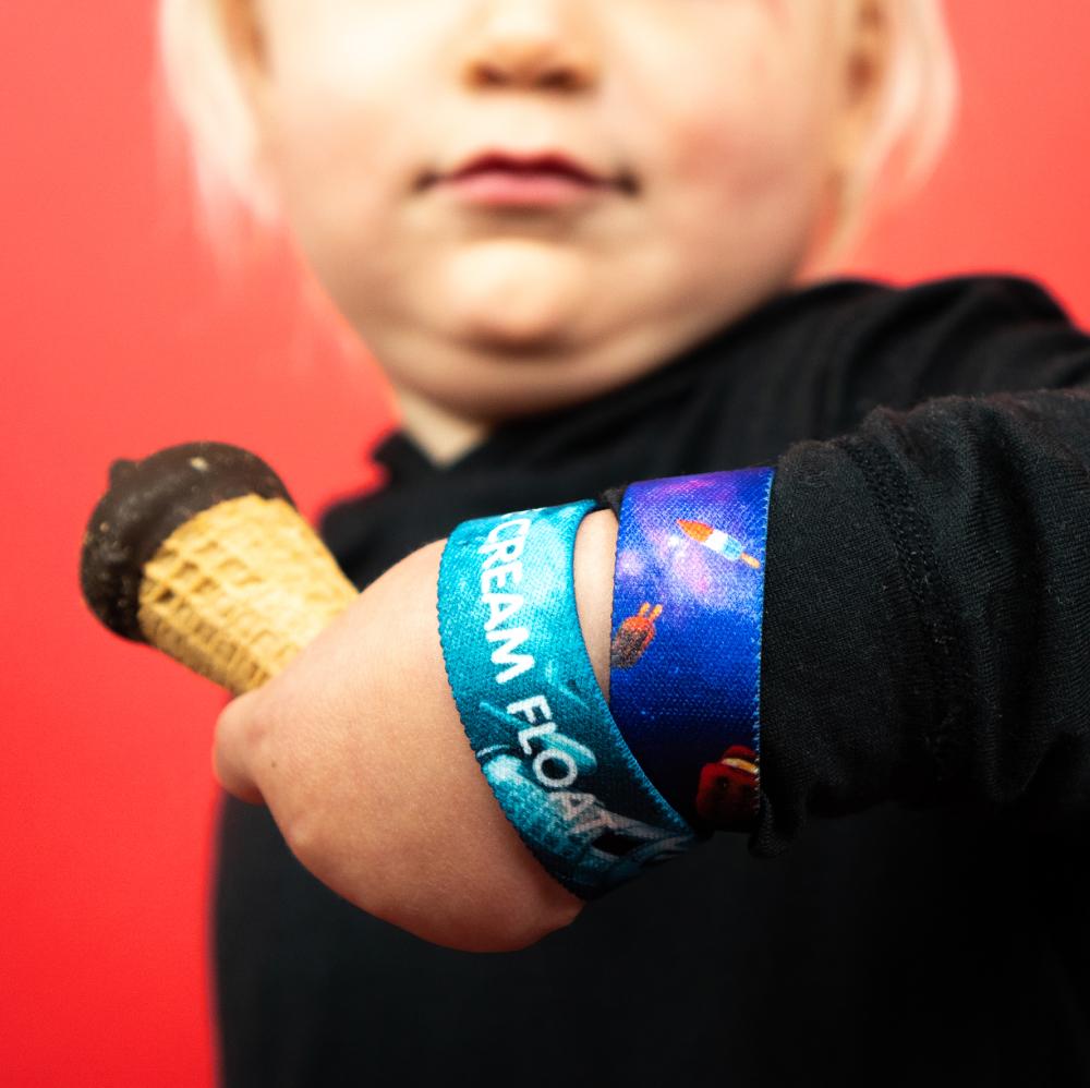 Studio photo of two Ice Cream Float straps on young boys wrist while he is holding an ice cream cone