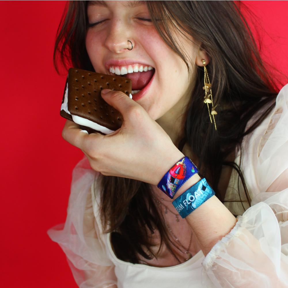 Studio photo of two Ice Cream Float straps on girls wrist while she is eating an ice cream sandwich