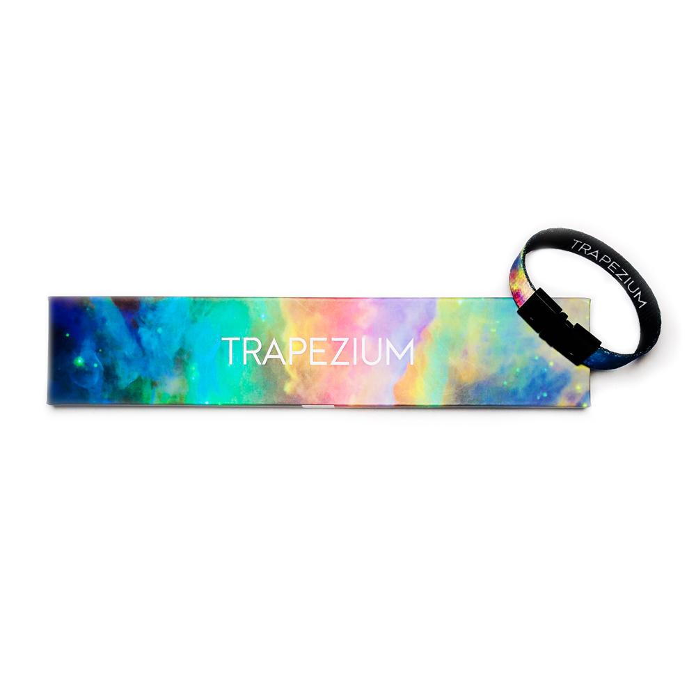 Studio image of Trapezium clasped together laying on the box it comes in, which has a design of  a multi-colored light space background and Trapezium centered in white text