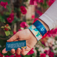 Close up image of hand holding a card with a quote on it and two Aquarius straps on their wrist