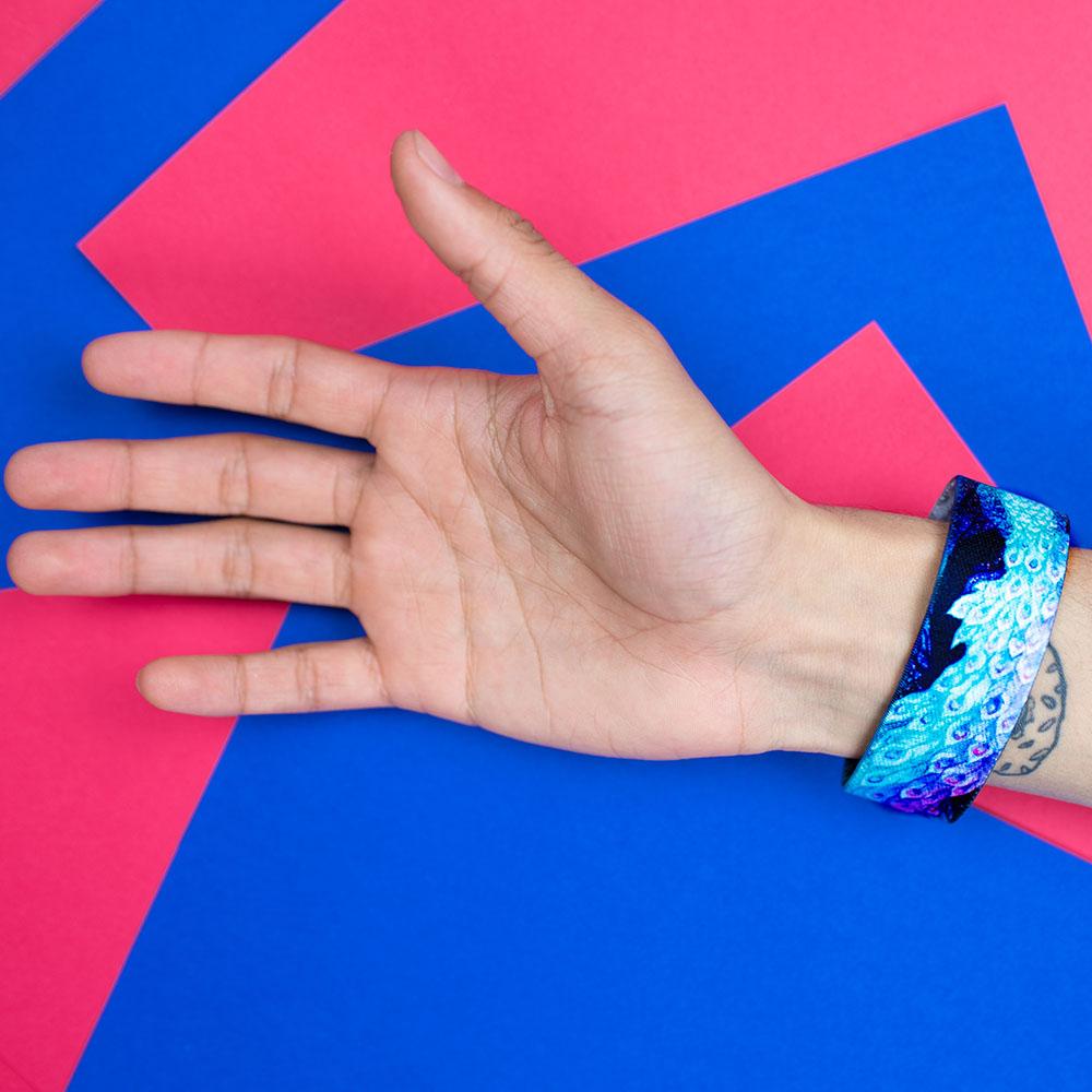 Studio Image of BeYOUtiful on a wrist with a geometric blue and pink-red background 