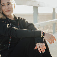 Lifestyle image of woman sitting with wrist crossed in front with Be The Light on one wrist