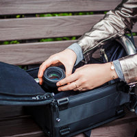 a lifestyle image showing a woman removing a lens from an opened up camera bag