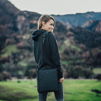a lifestyle image of a girl standing with the camera bag hanging from her shoulder overlooking the mountains.