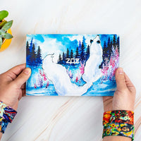 Studio image for outside of the custom envelope for the Fairies Pack held in hands that have two straps on each wrist from the pack. Design of the outside envelop is of a winter scene with a blue sky, trees, a few pink flowers, and a close up from behind of a sitting white fox