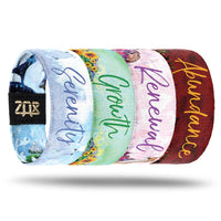 Inside designs of the four wristbands included in the Fairies Pack. From left to right. Light blue background with Serenity in dark blue text. Light green background with a few bundles of sunflowers on the bottom with Growth in dark green text. Light pink background with Renewal in dark pink text. Red background with Abundance in yellow text. All text is centered to each design.