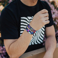 Lifestyle photo of guy wearing two find bigger problems singles one showing the inside design with bold text find bigger problems in a pink to yellow gradient with transparent neon geometric designs overlaying a black background above the single showing the outside design of find bigger problems with neon geometric design overlaying a black background