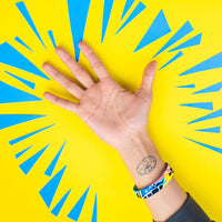 Studio photo of wrist in front of bright yellow background of fortune favors the bold single showing the outside design with hand drawn abstract art