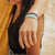 Lifestyle photo up close of guy's wrist wearing two guard your heart singles showing the outside design of guard your heart with mint, green, peach, pink, red, maroon, purple, blue rainbow design above another showing the  inside design with black text guard your heart with varying background in mint, green, peach, pink, red, maroon, purple, or blue