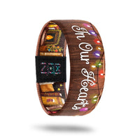 inside design for In Our Hearts. Brown wooden background with colorful lights across the top and In Our Hearts in white text at the center
