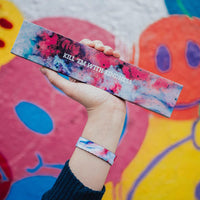 Lifestyle image of a hand holding a colorful box that says Kill 'Em With Kindness and wearing the Kill 'Em With Kindness imperial