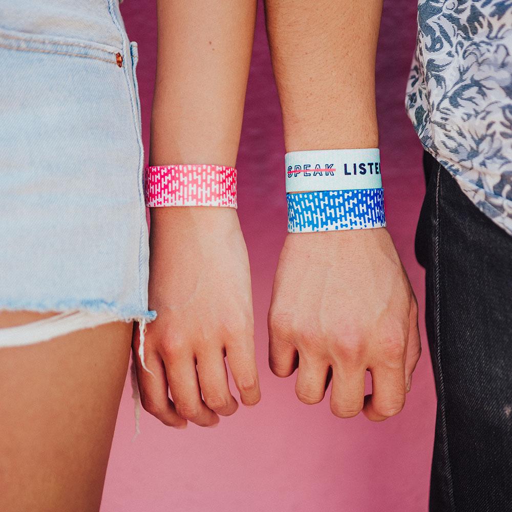 Studio image of a wrist wearing 1 Listen and the other wrist is wearing 2 Listen wristbands