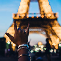 Lifestyle close up image of a hand in front of the Eiffel Tower wearing Never Give Up