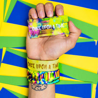 Studio Image of hand holding card that says Once Upon A Time with 2 Once Upon A Time straps on their wrist in front of a colorful background