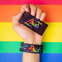 Studio Image of hand holding card that says Pride with a Pride strap on their wrist