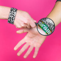 Studio image of a hand, wearing a Release Your Inner Awesome and holding a magnified glass over 2 Release Your Inner Awesome on someone else's wrist 