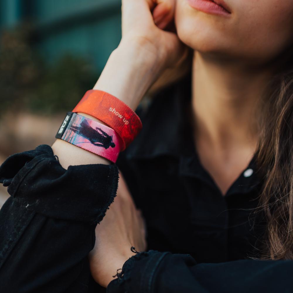 A lifestyle photo of a woman wearing two Show Up wristbands at the same time. One showing the inside and the other showing the outside while her hand is near her jaw