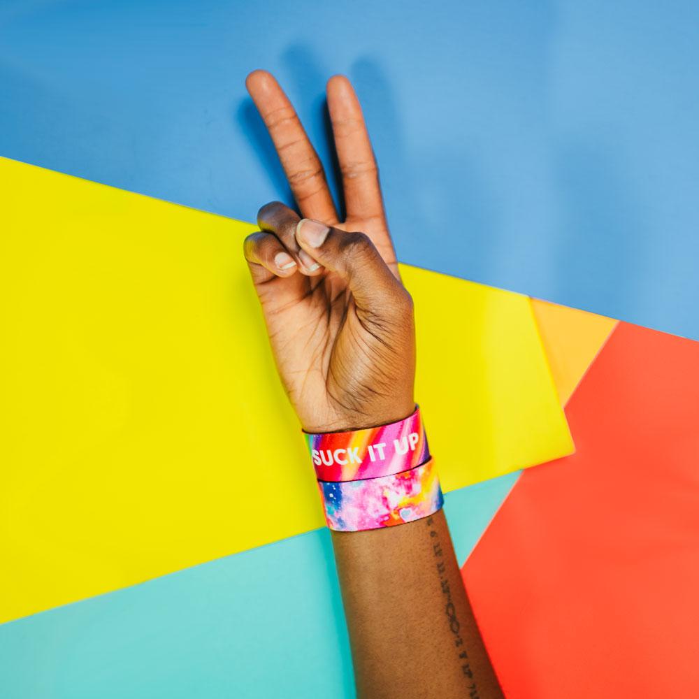 Studio image of hand peace sign and 2 Suck It Up on wrist