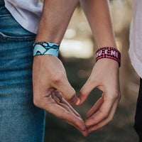 Models are forming a heart with their hands while one is wearing a blue You & Me and the other is wearing a pink You & Me