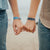 Lifestyle image of hands interlocked at their pinky fingers while both are wearing You Are Enough on their wrist